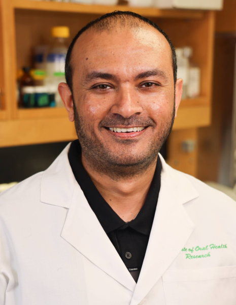 Man with black hair wearing a white coat smiling in a lab setting